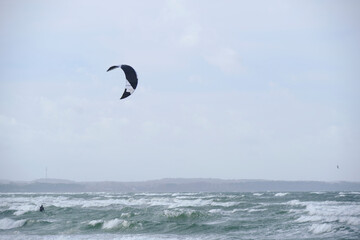Kitesurfing, riding board waves during storm holding to flying kite.