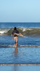 Man carrying a surf board into the water at the beach in Tamarindo, Costa Rica