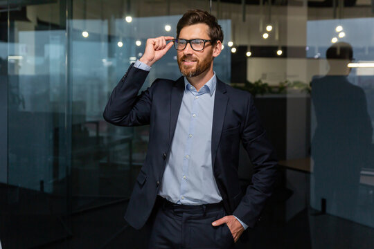 Portrait Of Successful Businessman Mature Boss In Business Suit, Man Working Inside Office At Work In Glasses Looking Away, Senior Investor With Beard Smiling And Dreamy.