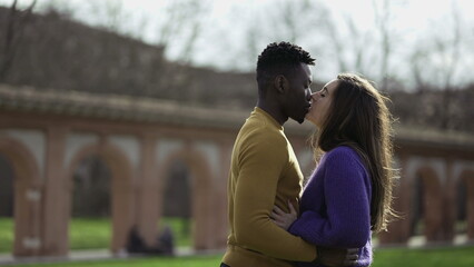 Fototapeta premium Black man kissing white girlfriend standing outside at park
