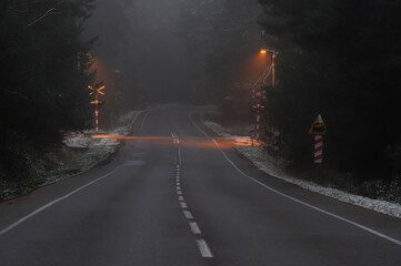 Railway crossing across the road in a foggy forest in winter time