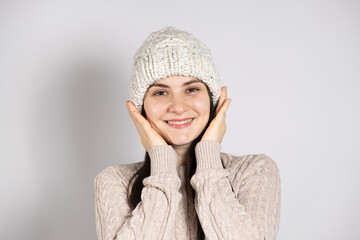 A happy brunette woman in a winter hat and a knitted sweater smiles on a white background.