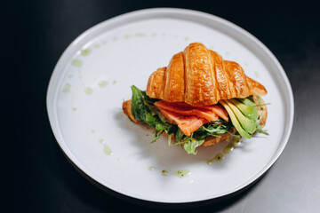Croissant with salted salmon and avocado slices on white plate, top view. Cooking healthy breakfast concept.