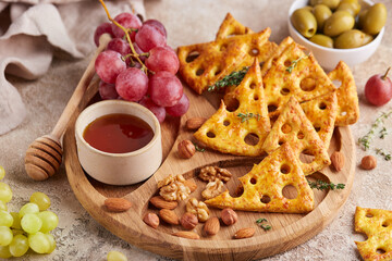 Cracker cookies styled as pieces of yellow cheese with holes. Savory snack served with honey and grapes. Delicious homemade appetizer for wine.