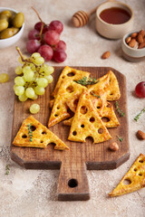 Cracker cookies styled as pieces of yellow cheese with holes. Savory snack served with honey and grapes. Delicious homemade appetizer for wine.