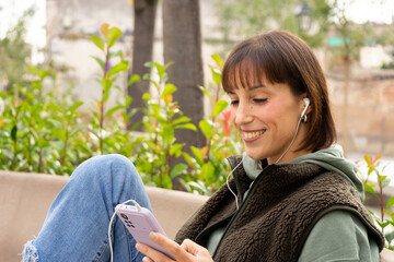 happy girl. Girl sitting in a park relaxed while she sends messages and listens to music	