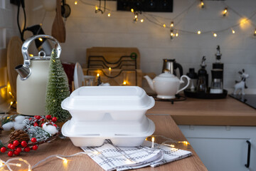 Food delivery service containers on table white scandi festive kitchen in christmas decor. Eve New year, saving time, too lazy to cook, hot order, disposable plastic box in fairy light. mock up