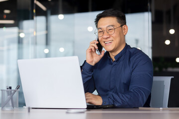 Successful Asian man smiling and talking on the phone, businessman in a shirt working inside the office using a laptop.