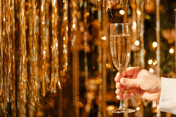 Champagne glass in mans hand against luxury glow golden rain decoration expensive holidays party