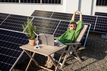 Woman works on laptop while sitting relaxed by the table on rooftop with a solar power plant....