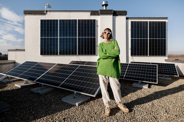 Portrait of a happy woman stands on a rooftop with a solar power plant installed on it. Happy owner...