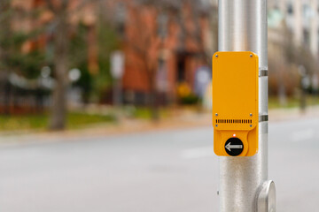 Yellow pedestrian push button sign on traffic signal pole at crossroad in street in Canada