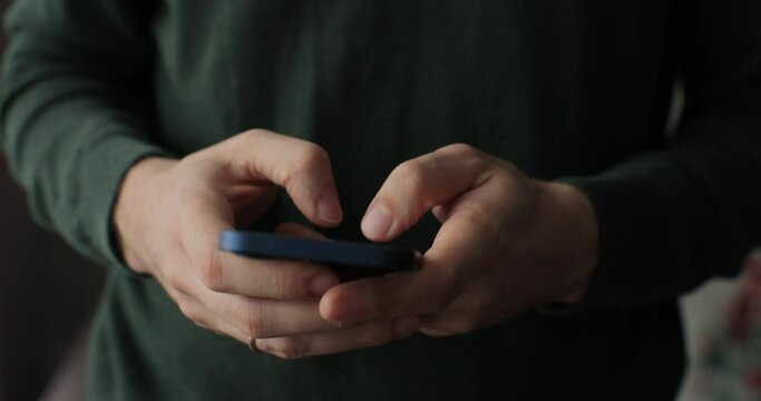 Male texting at phone in living room. Online shopping, browsing the internet and checking videos on social media. Close-up.