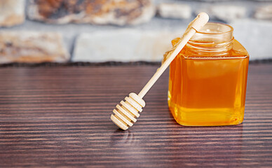 a jar of honey with a wooden dropper on a dark wooden table