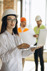 Woman engineer standing with laptop with contractor workers on the background