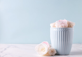 Light blue cup and  white roses flowers  in it on white marble background against blue wall. Selective focus. Place for text.