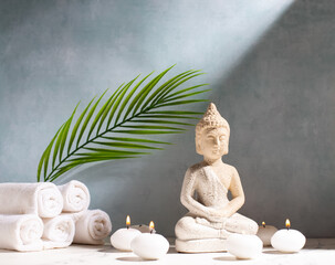 Calming spa setting. Buddha and burning small white candles against blue textured wall. Wellbeing time concept. Place for text.
