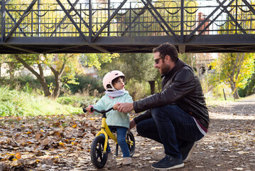 Fototapeta premium Father teaching her little daughter to ride a balance bike in a park.