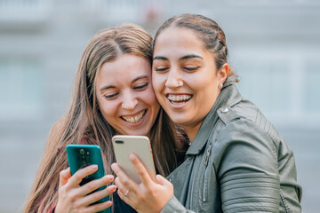 Fototapeta premium friends with mobile phones smiling hugging in the street