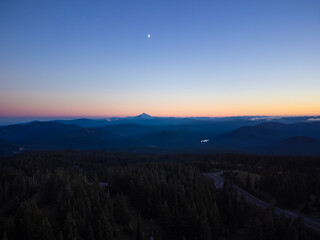 Twilight. Pine forest, mountain range and highway. The sky is colored orange by the rays of the setting sun. Beautiful nature. Tourism, travel, ecology.