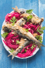 Marinated  sardines or Sarde in saor, a typical dish from the Venice, Italy  with white onions marinated with beetroot and vinegar, raisins and pine nuts. Blue wooden background - 548861018