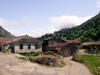 Vistas de las casas del pueblo de  Villar de Vildas, con las montañas verdes al fondo, cielo azul y callejuelas, en verano de 2021 , Asturias, España.