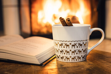 Cup with cinnamon and book in front of fireplace