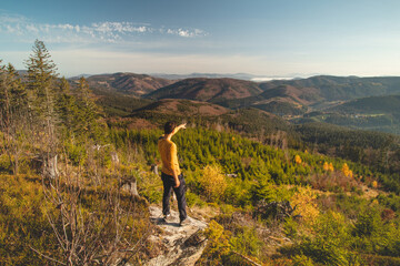 Enthusiastic traveller stands on a rock, looking down into the valley. Happy to have reached destination. The backpacker points to his next destination. Beskydy mountains, Czech Republic