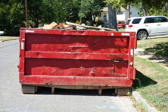 End view of a large red beat up dumpster on the street by a curb in a residential development