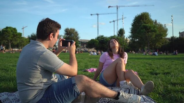 young caucasian woman and man student friends relaxing, having fun in the park and taking photos