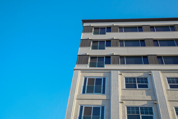 An upward partial view of a tall concrete building with lots of double hung windows.  A grey cloudy sky is a background to the condo building. The textured exterior walls are of two tones of grey. 
