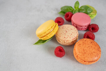 Sweet colorful macarons with berry filling and raspberries on a gray background with copy space. French meringue cookies macaron. Confectionery and berries.