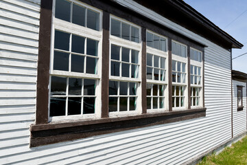 An exterior wooden white vintage building with dark brown trim and a row of windows. The wood wall...