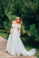 Fototapeta premium a blonde bride on a path in the park in a white long dress.