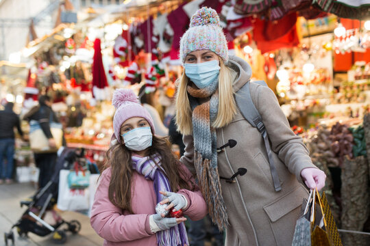 Portrait of happy family in protective masks after shopping for gifts - daughter hugs mom at street market