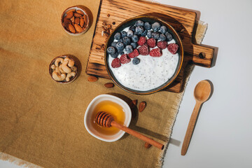Yoghurt in green plate with blueberries, raspberries and chia seeds on the white table lined with a beige tablecloth. The concept of healthy eating. Flat lay