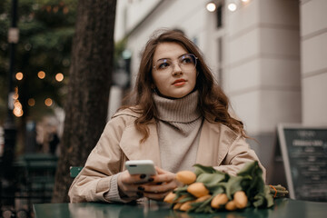 Beautiful girl with tulips and phone sitting at a table. Girl with yellow tulips with smartphone.