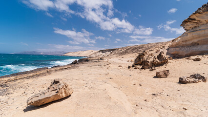 Fototapeta na wymiar Scenic sandy desert coastline surface with view of turquoise ocean and hill elevations in distance, Fuerteventura, Spain