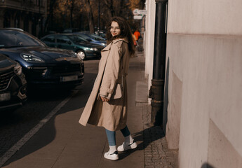Obraz premium Young woman in a coat outside. Outdoor autumn portrait of young elegant fashionable woman wearing trendy glasses, camel color coat, shoulder bag, walking in street of European city. Copy space