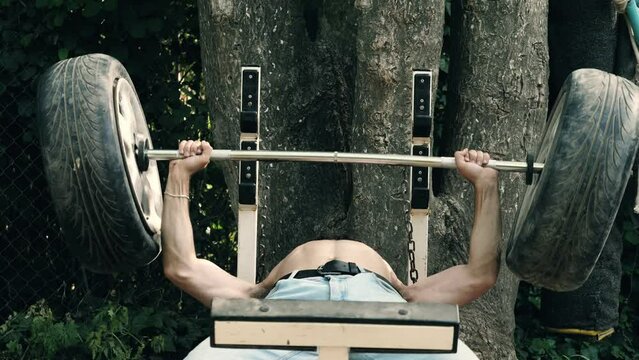 training, fitness - young man at the park lying on the bench lifts weights