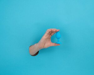Woman holding a blue anal plug on a blue background. 