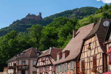 houses of a village in Alsace with a castle in the background and some green mountains.