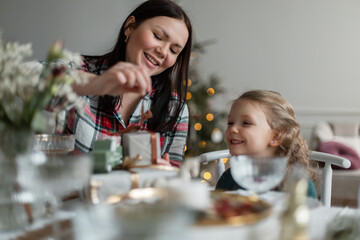 Happy mother with her child daughter sit at the festive table and give gifts on Christmas Eve