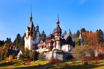 Fototapeta premium View of Peles castle with arranged courtyard and colorful autumn forest in Sinaia, Romania, Europe