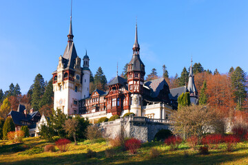 Fototapeta na wymiar View of Peles castle with arranged courtyard and colorful autumn forest in Sinaia, Romania, Europe