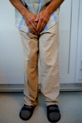 man in beige trousers with trickle of urine, male hands on groin, mature man wants to go to toilet,...