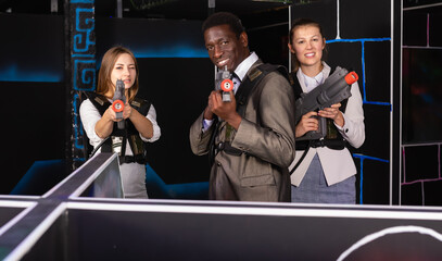 Fototapeta na wymiar African man and two glad European female in business suits at laser tag room