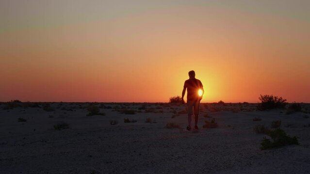 Silhouette of a man walking toward camera in desert with sunset behind. Male tourist catching the sunset in Sahara. Travelling concept.