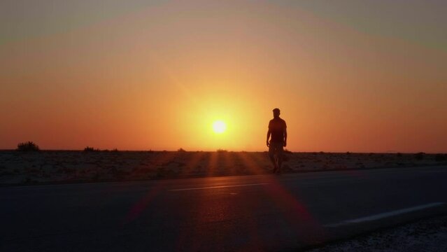 Large shot of a man walking along the road with a sun set in the background. Sunset light in the dark and a man silhouette having a walk in sahara.