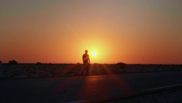 Man walking along the road with a sun set in the background. Sunset light in the dark and a man silhouette having a walk in sahara.